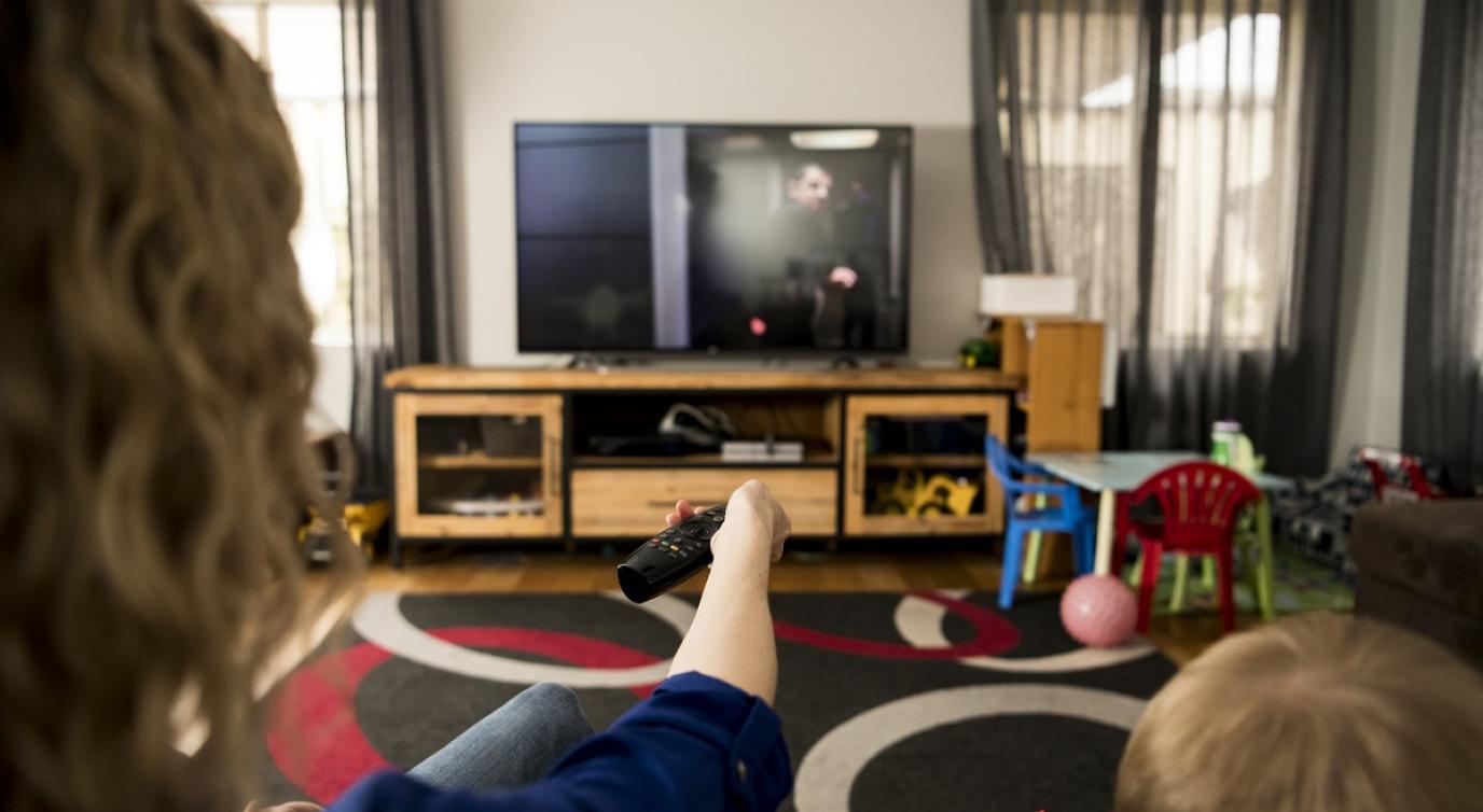 A mother and child sitting on a couch holding a remote up to the TV